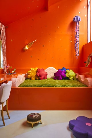 An orange bed frame extends from a wall of the same orange color green bedding desk and white chair to left purple...