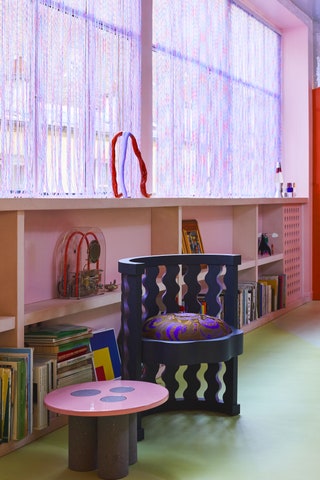 Purple and pink shades line a window above open pink shelving small pink table and purple chair in foreground