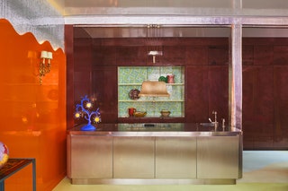 stainless steel island in front of wine colored wall with builtin shelving orange wall to left