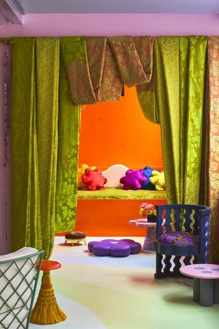 Orange alcove space with green bench lined with bright pillows framed by green drapes