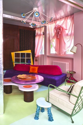 purple and red sofa with orange pillow pink walls with pink curtains drawn up at center chandelier with blueandwhite...